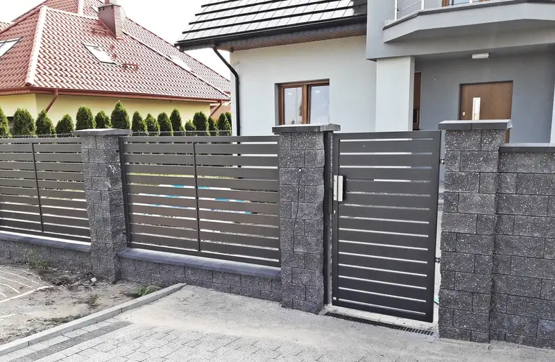 Ogrodzenie z poziomych profili między słupkami z bloczków łupanych